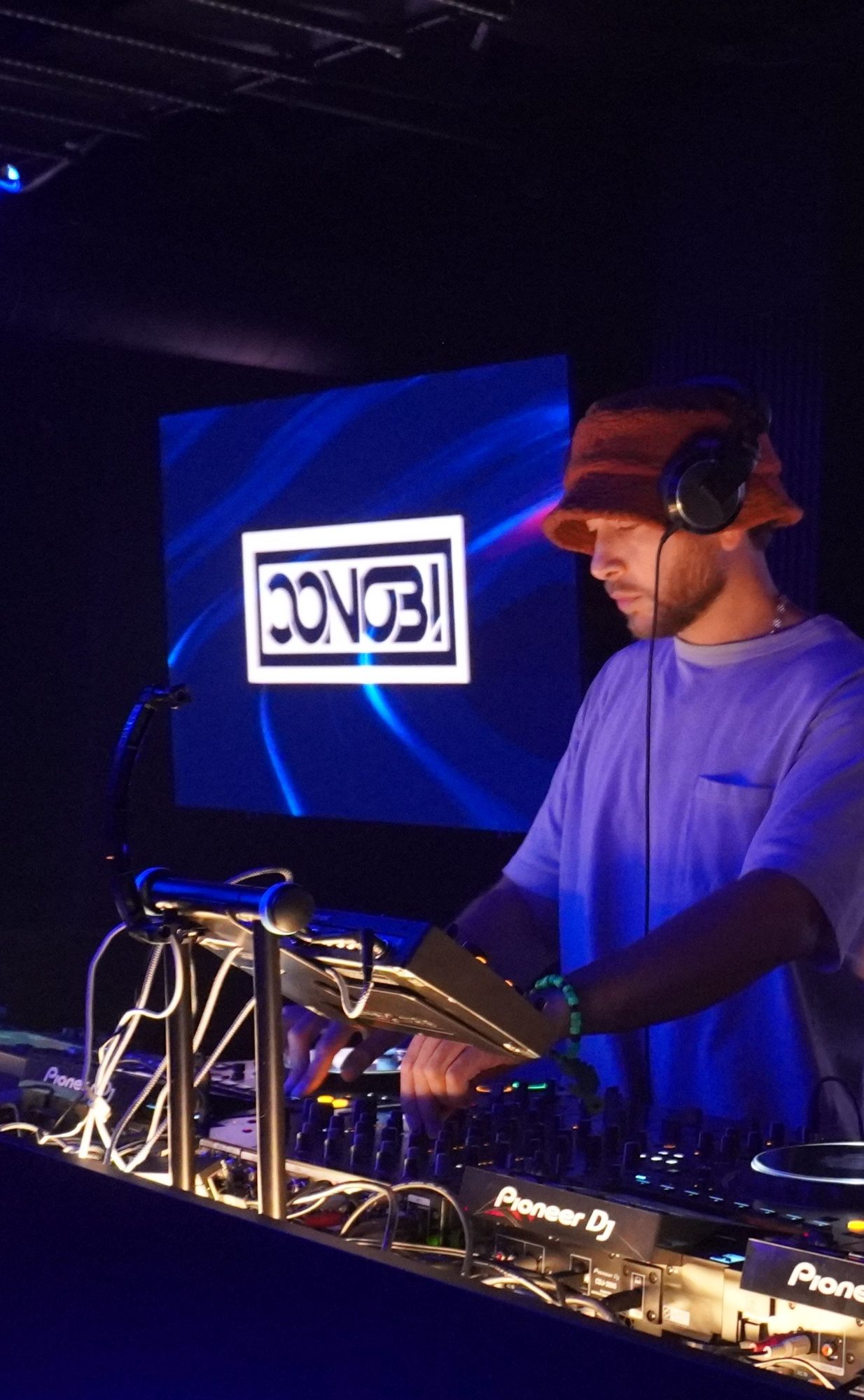 Conobi mixing in a bucket hat with the Conobi logo on the screen behind him