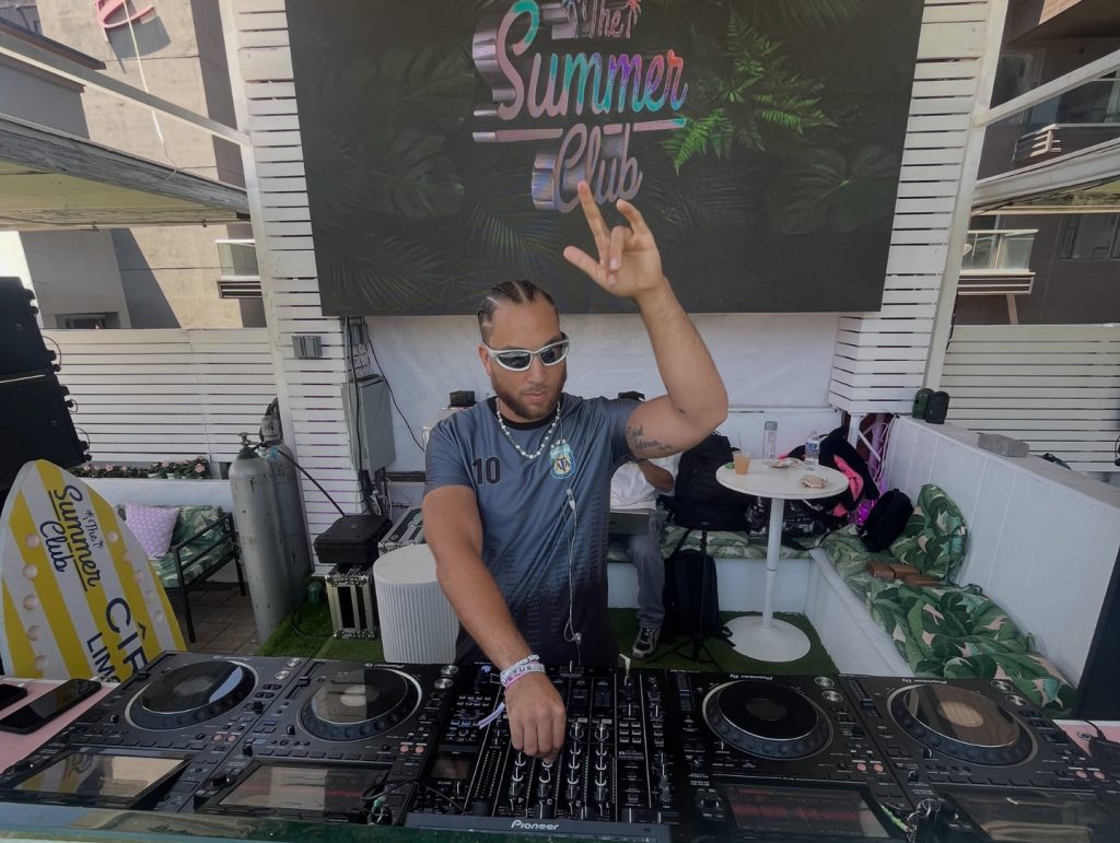 Conobi with a hand in the air behind the decks at Summer Club